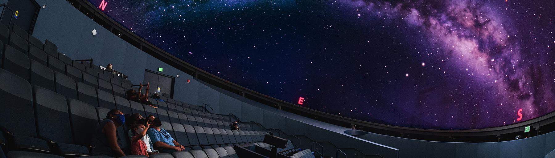 State Museum Planetarium with guests seated and one young girl pointing up at the milky way projected on the dome