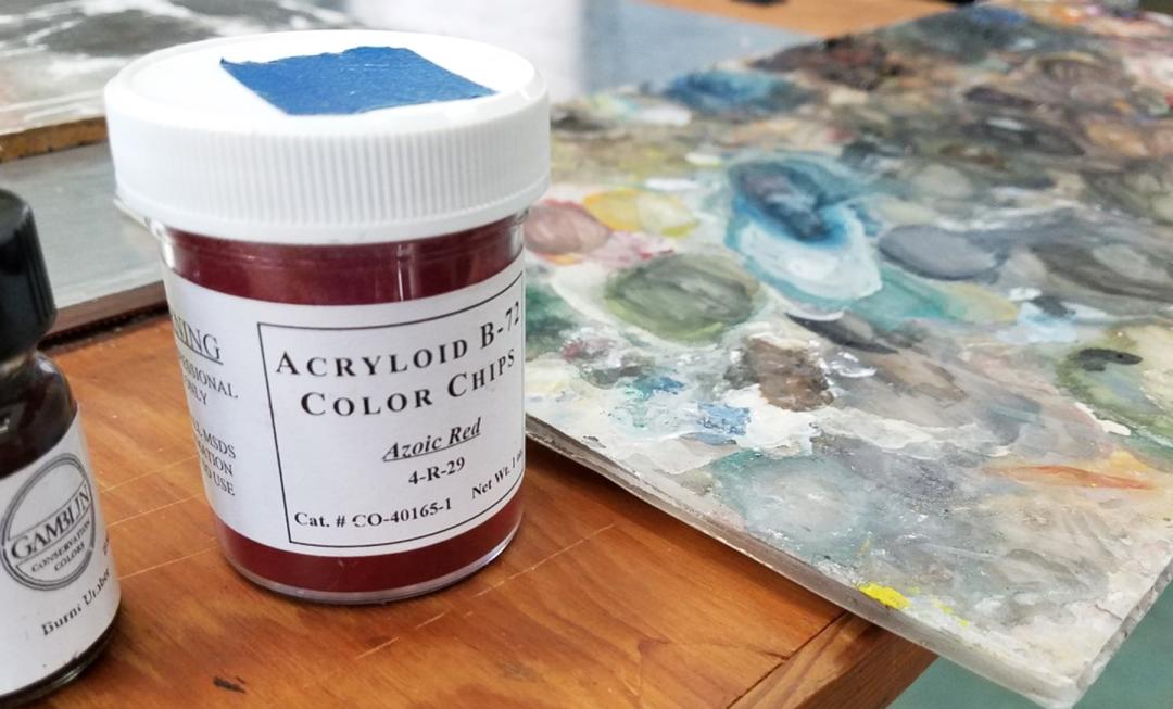 A jar of azoic red color chips sits on a table next to a painting