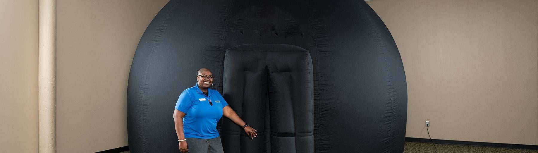 Woman in blue shirt stands in front of entrance to large black inflatable dome