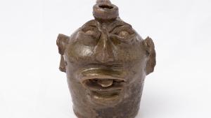 Small ceramic jug with image of face fashioned into its side with its tongue sticking out
