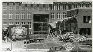 Black and white image of long, four story textile mill building under renovation. A sign is posted in front promoting the 5.6 million dollar project.