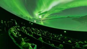Audience looks up at domed shaped image depicting bright green lights in the sky over a snowy landscape