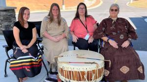 Four women sit in a semi circle around a large drum