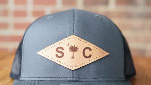 Baseball Cap with Dark Gray Front and Brown Leather Diamond Shaped Patch with Palmetto and Crescent and SC Lettering