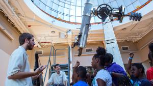 Museum observatory educators speak to a group of students with the observatory telescope in the background