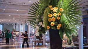 Large vase of yellow flowers and palm fronds with the State Museum's Main Lobby in the background.