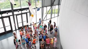 Looking down on a group of students standing in the planetarium lobby with paper mobile artwork hanging from ceiling