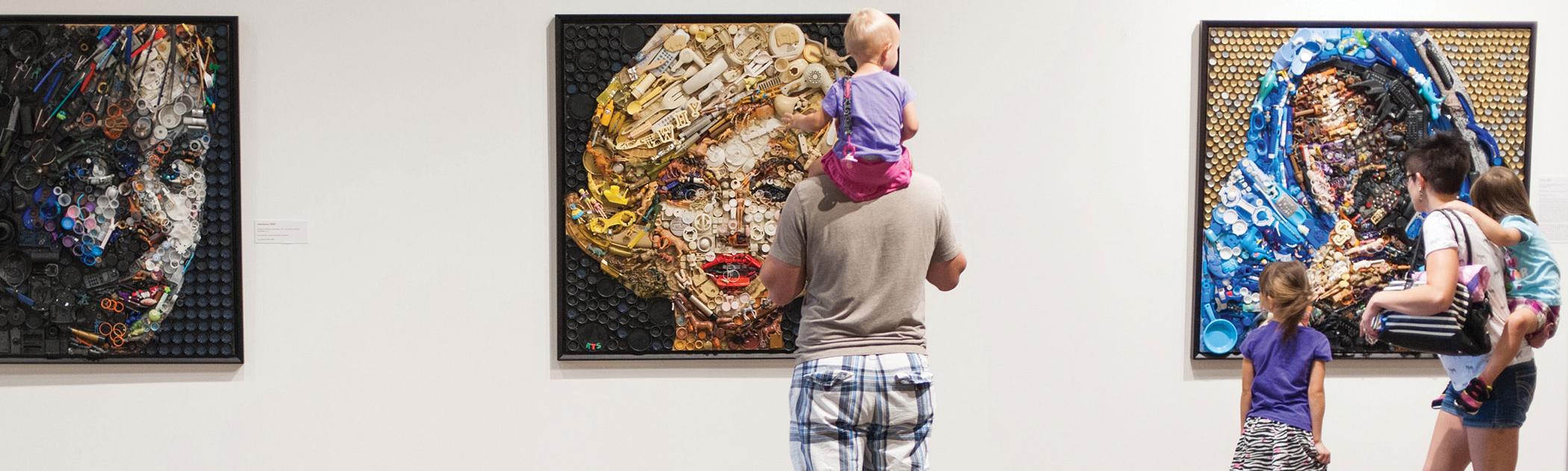 Family looks at 3 pieces of art displayed on a wall, including a portrait of Marilyn Monroe