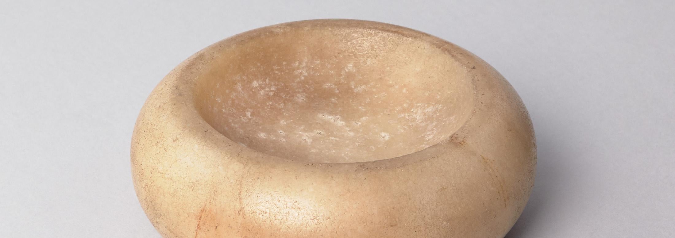 Round pale yellow or ivory colored stone disc with divet carved into the center 