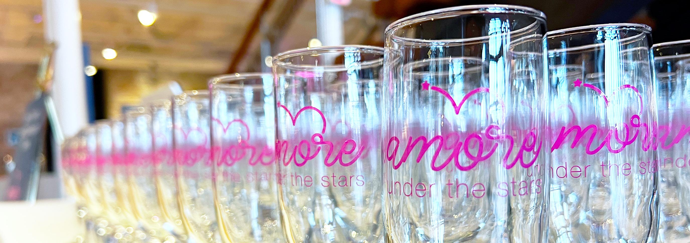 Glass Champagne with a logo in pink that reads "Amore Under the Stars" site lined up for display.