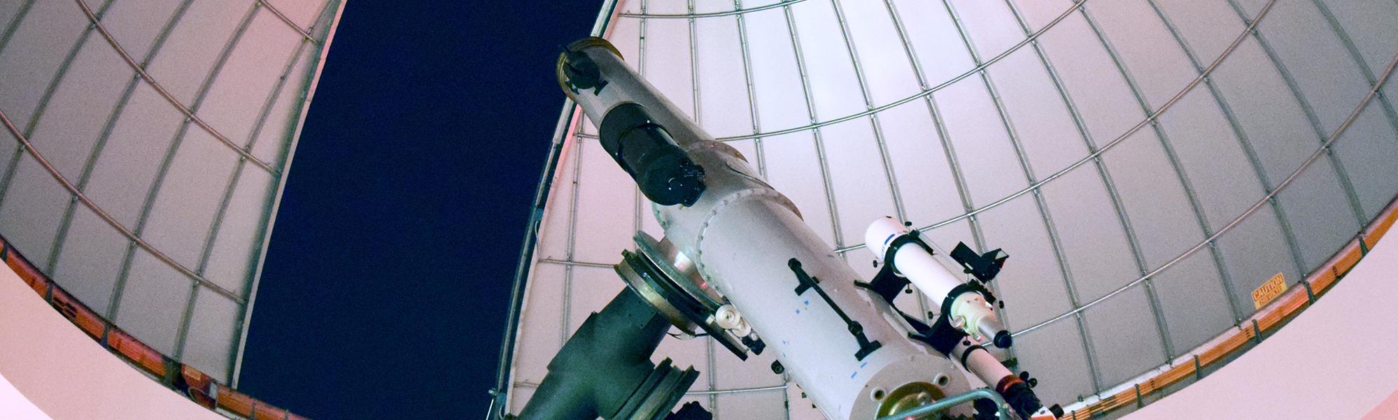 Large white telescope points towards the dark night sky under a partially open observatory 