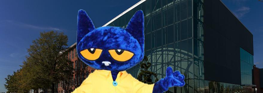 Mascot cat with large blue head wearing a yellow shirt stands at museum entrance