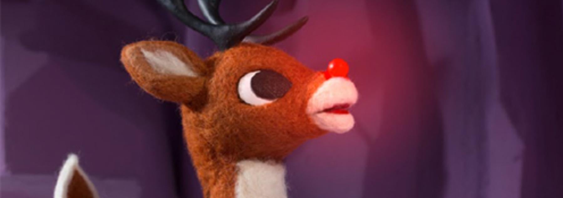 Rudolph the Red Nosed Reindeer with glowing nose stands against a purple background.