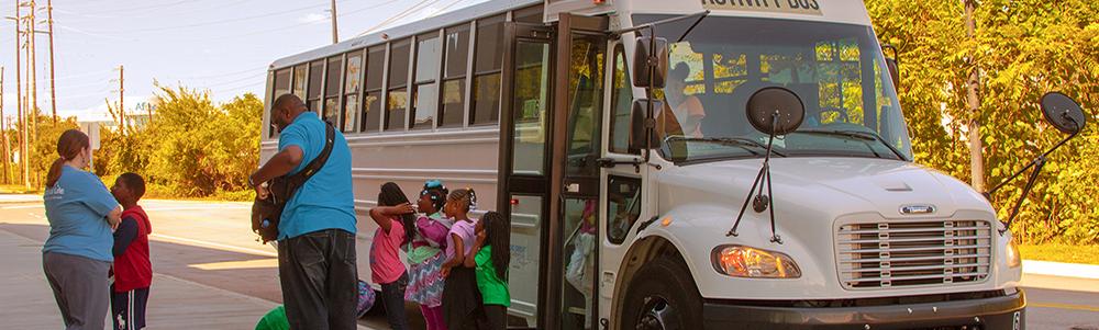 Group of small students and two adults exits a white bus parked next to the South Carolina State Museum