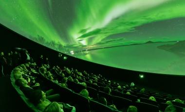 Audience looks up at domed shaped image depicting bright green lights in the sky over a snowy landscape