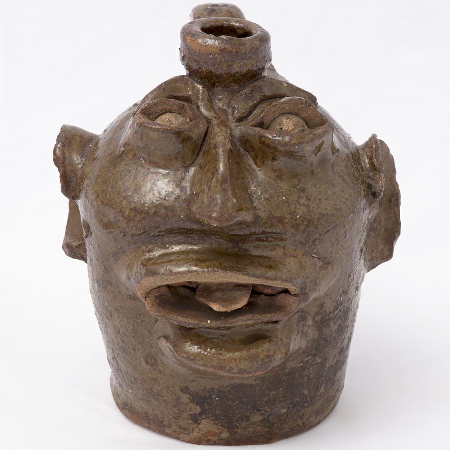 Ceramic vessel in the shape of a face with large ear and a protruding tongue