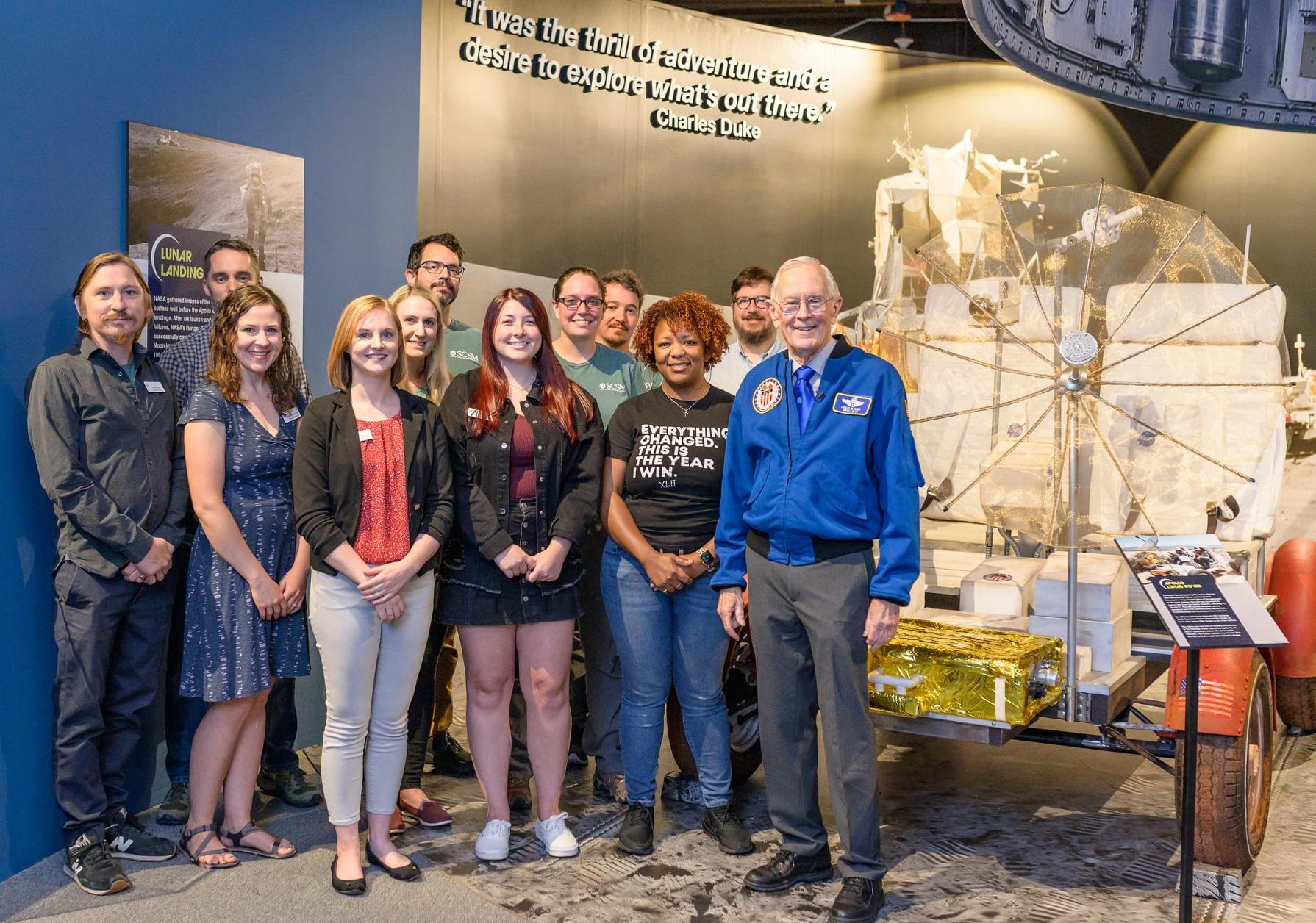 Museum Exhibition and Collections staff pose with Gen Charles Duke in the Apollo 16 and Beyond exhibition.