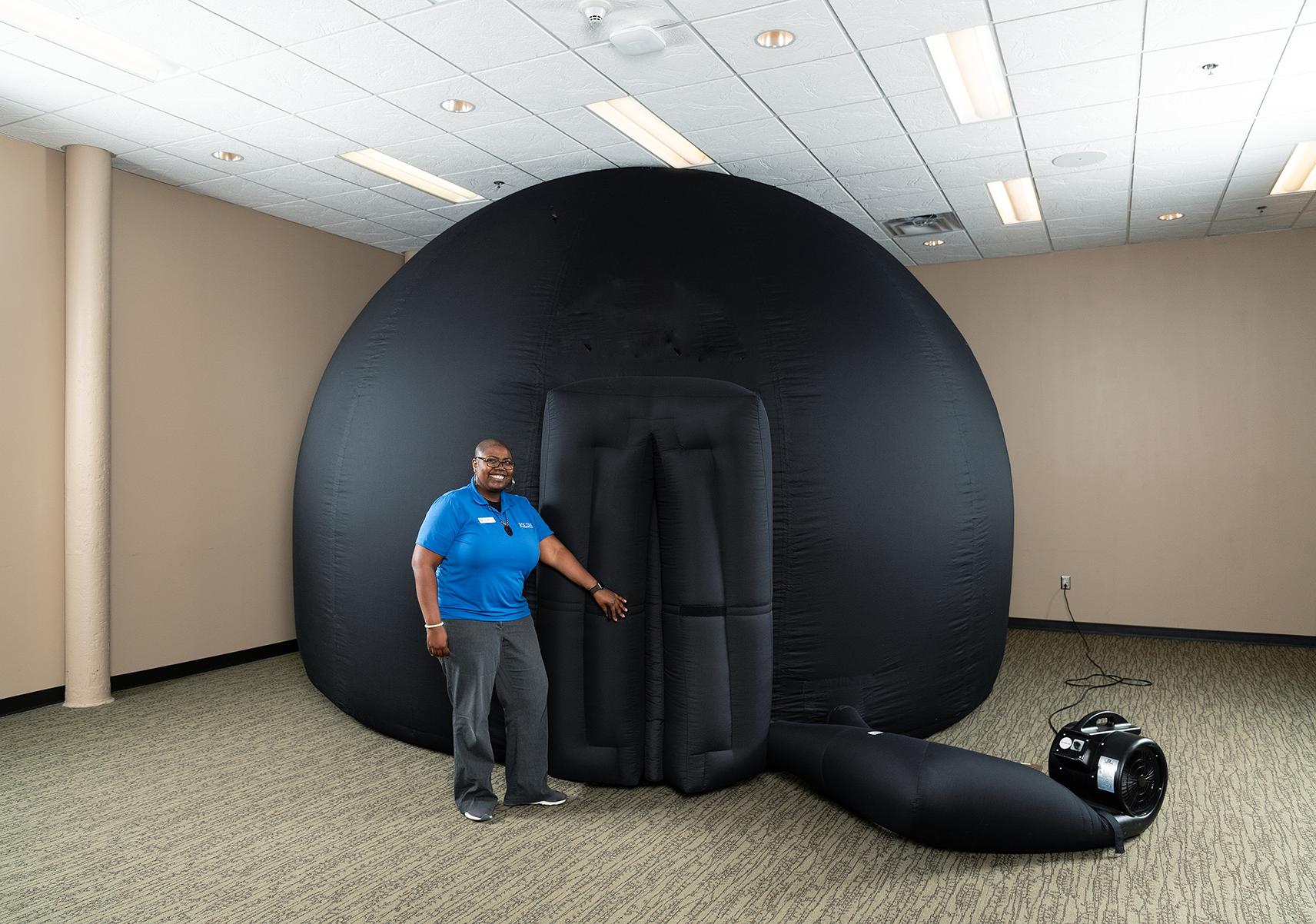Woman in blue shirt stands in front of entrance to large black inflatable dome