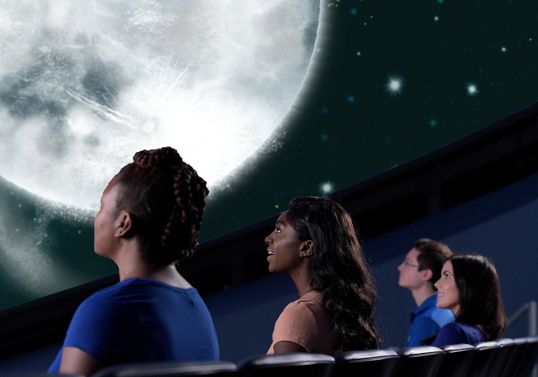 Individuals seated in theater looking up at an image of the moon