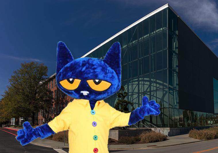 Mascot cat with large blue head wearing a yellow shirt stands at museum entrance