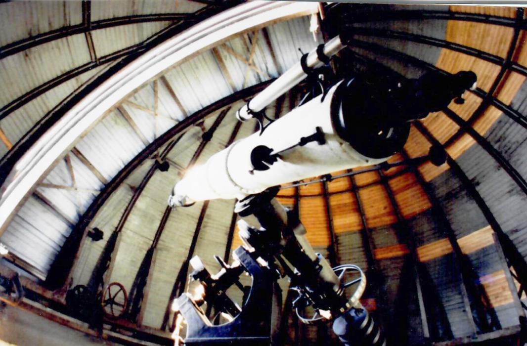 White telescope points up at closed, wooden observatory dome that is not the best shape with section unpainted and peeling in areas.
