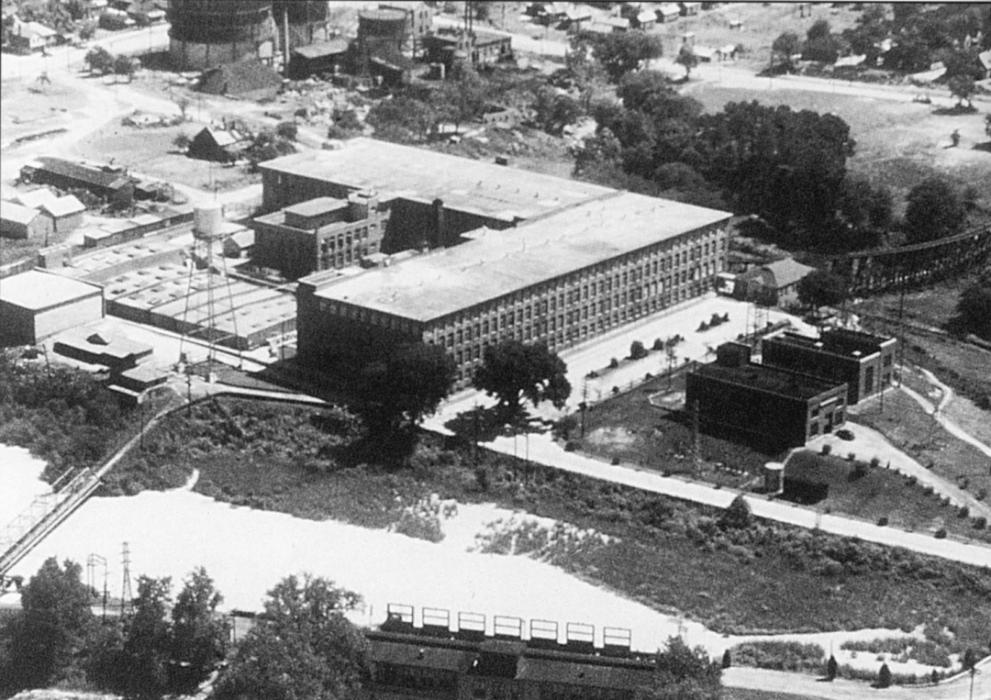 Arial views shows large 'L' shaped brick building with canal alongside it