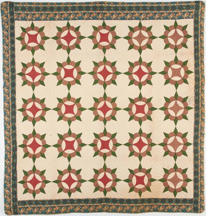 a quilt with a multi patterned border and red and green star bursts on a cream colored background