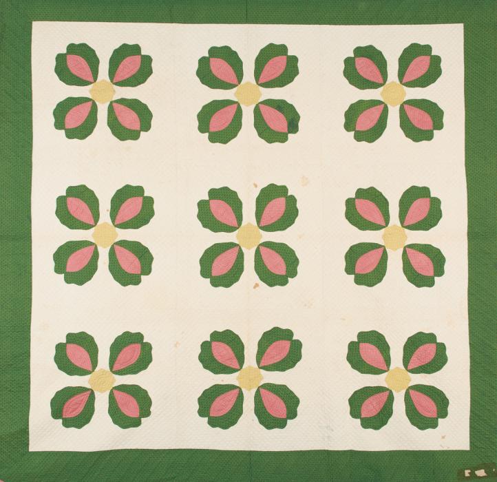 Quilt with green border and cream center with repeated motif of four petal flower in green and pink with yellow center