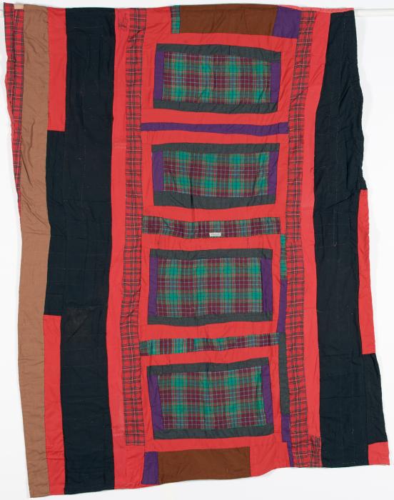 Quilt made of solid panels of red and black with green plaid rectangles featured down the center.