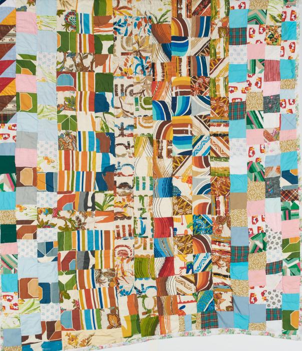 Quilt made of many small fabric scraps pieced together in stripes, solids, swirls and abstract patterns. Colors are a mix of blue, pink, brown, green, orange and yellow.