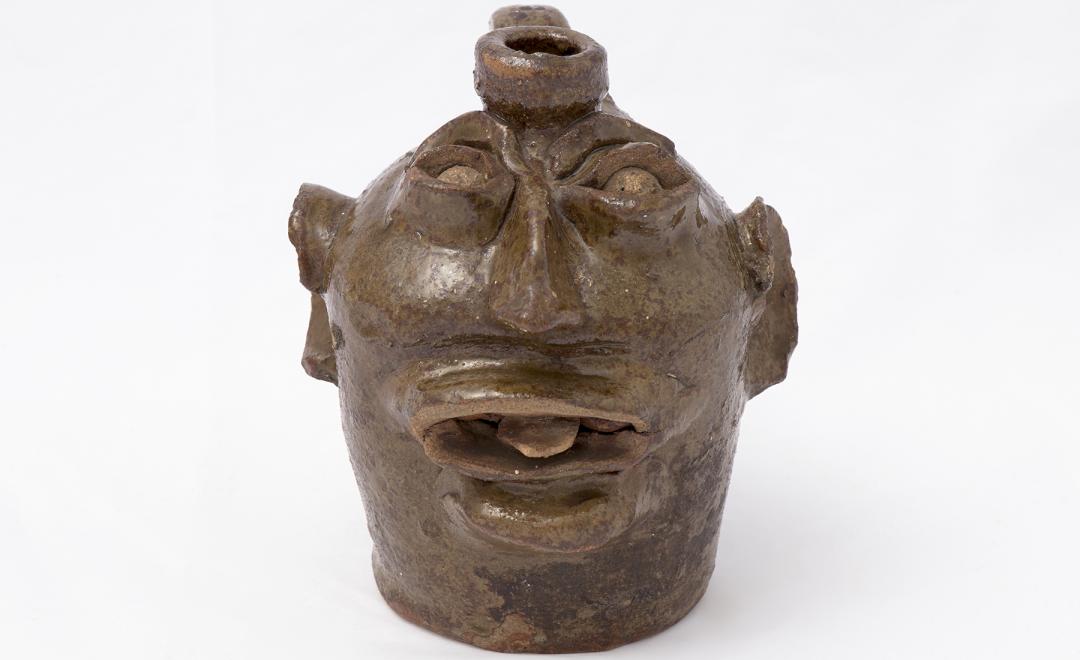 Ceramic vessel in the shape of a face with large ear and a protruding tongue