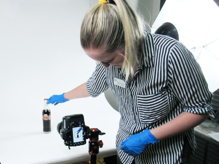 Individual wearing gloves setting up a bottle of pop to be photographed