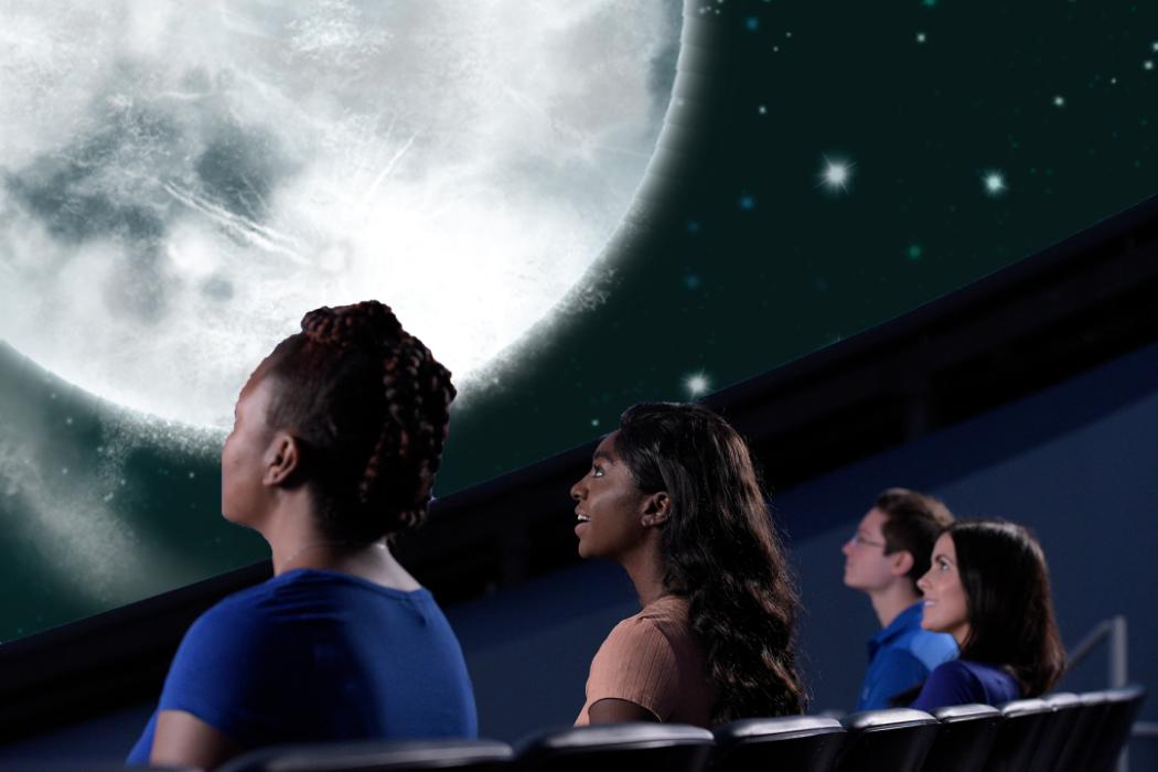 Individuals seated in theater looking up at an image of the moon